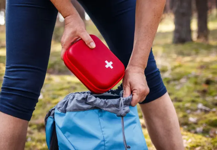 Person packt roten Erste Hilfe Set Inhalt in blauen Rucksack für Wanderung.
