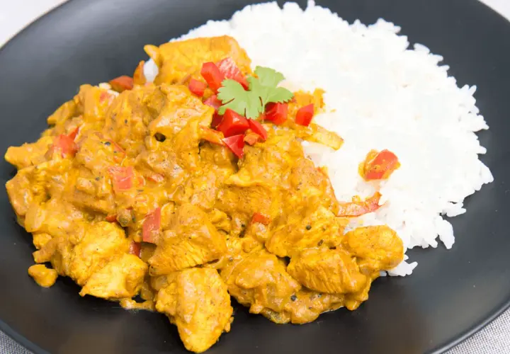 Aromatyczny kurczak curry z ryżem, doprawiony papryką i świeżą kolendrą, podany na czarnym talerzu.
