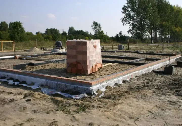 Stan zero budynku: fundamenty z cegły i betonu, stos materiałów budowlanych.