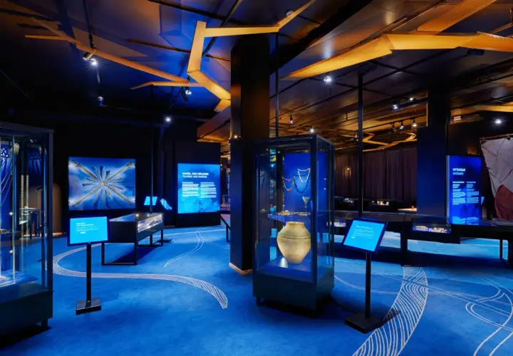 En utställning om historiska museet vikingar. Blå matta med vita mönster, montrar med föremål och skärmar med information.
