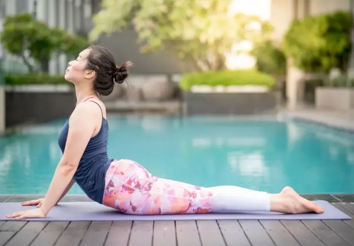 Kobieta w pozycji bhujangasana na macie przy basenie, zrelaksowana, z głową uniesioną do góry.