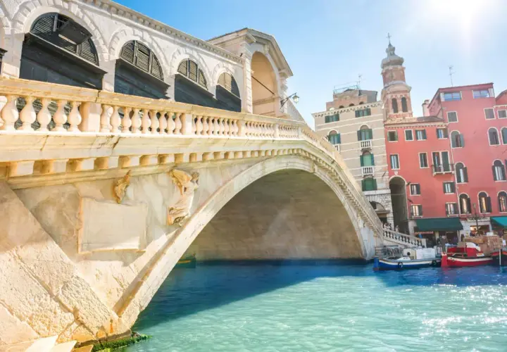 Le célèbre pont du Rialto à Venise, avec ses arches majestueuses et ses bâtiments colorés en arrière-plan, se reflète dans les eaux turquoise du Grand Canal.