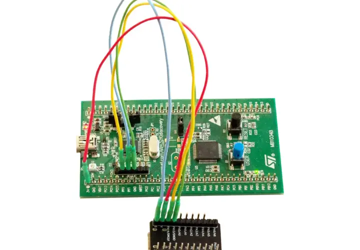 Zielona płytka STM32 z kolorowymi przewodami podłączonymi do małego modułu.