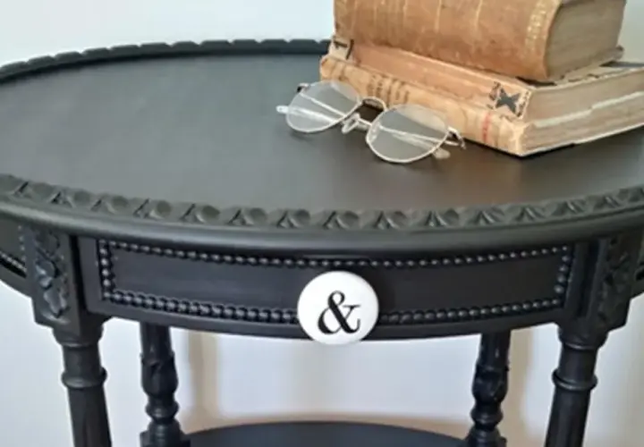 Come trasformare un vecchio comodino in un pezzo d'arredo chic: un tavolino nero con pomello a "&" e libri antichi.