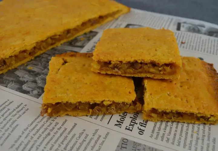 Coca amb tonyina, un delicioso pastel salado relleno de atún y cebolla, servido sobre un periódico.