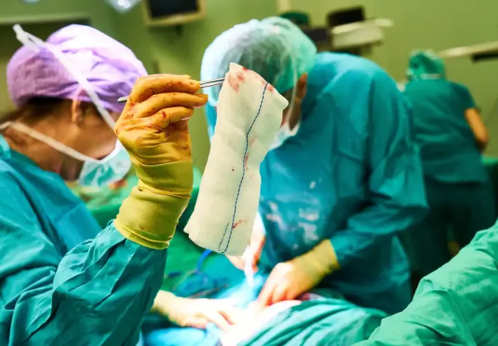 Chirurghi in sala operatoria. La mano guantata tiene una garza insanguinata, un dettaglio che potrebbe far pensare alle tabelle risarcimento malasanità morte.