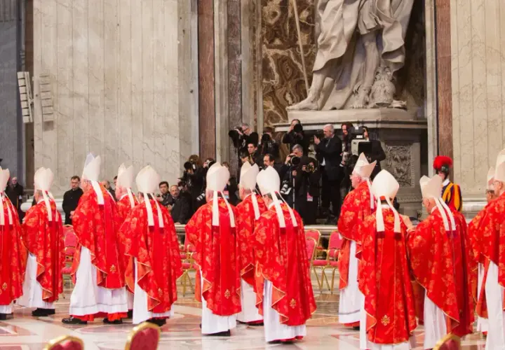 Kardinäle in roten Gewändern und Mitra stehen in einer Kirche. Dies ist ein Moment, der an ein Konklave erinnert, wo ein neuer Papst gewählt wird.