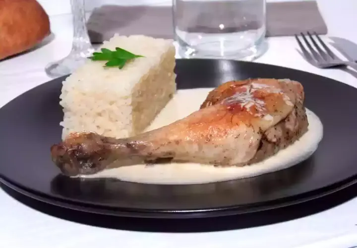 Un délicieux poulet à la crème, servi avec une portion de riz blanc et une feuille de persil. Un plat savoureux et réconfortant.