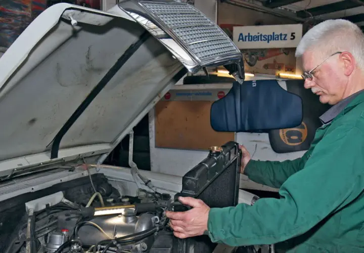 Mechanik w zielonym kombinezonie wykonuje wymianę chłodnicy krok po kroku w warsztacie.