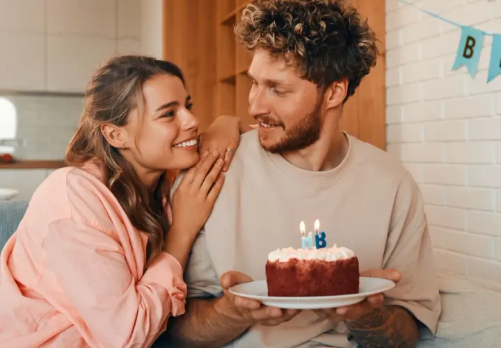 Pareja sonriente celebra un cumpleaños con un pastel. Ideas de frases bonitas para felicitar cumpleaños a tu pareja.