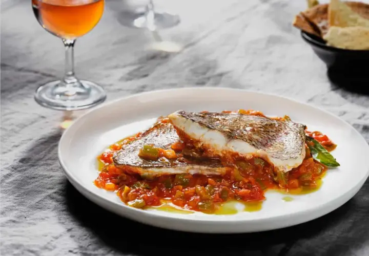 Deliciosa urta a la roteña servida en plato blanco, con vino y pan tostado al fondo.