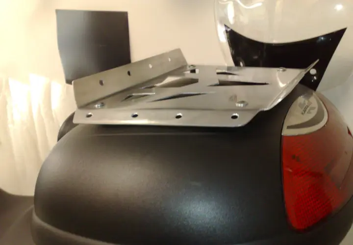 Piatto metallico forato, parte di un portapacchi moto fai da te, fissato su un bauletto nero.