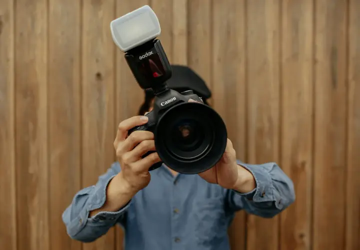 Fotograf trzyma aparat Canon z lampą błyskową Godox. Liczba przewodnia lampy błyskowej jest kluczowa dla uzyskania idealnego oświetlenia.