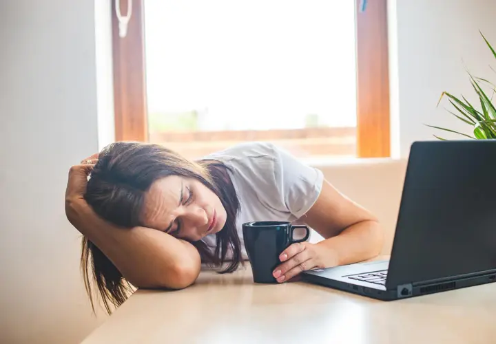 Donna esausta con tazza e laptop, forse cerca rimedi della nonna per la carenza di ferro.