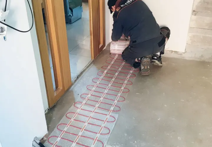 Instalator układa matę grzewczą, przygotowując podłogę do montażu. To inwestycja w komfort i przyszły koszt ogrzewania podłogowego.
