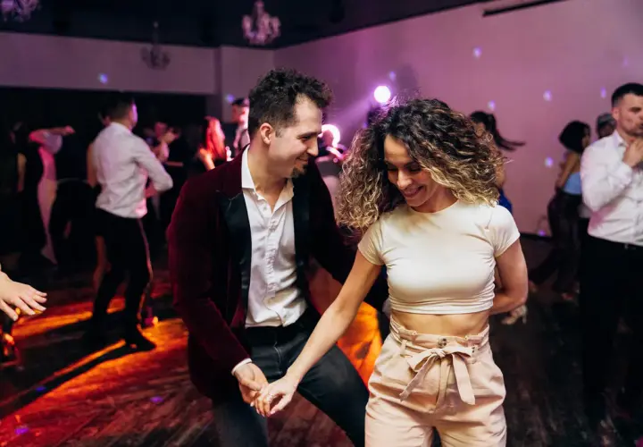 Para tańczy w rytm muzyki, ciesząc się wspólnym tańcem użytkowym. W tle widać innych bawiących się ludzi.
