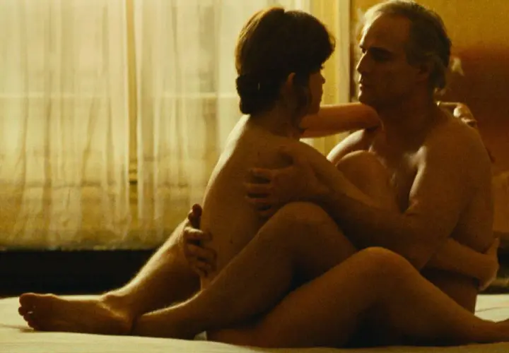 Una scena intima di sesso al cinema, con una coppia abbracciata in un letto, illuminata da una luce soffusa.