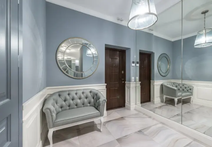 Elegancki, duży reprezentacyjny przedpokój w pałacu z szarą kanapą, ozdobnymi lustrami i dwoma drzwiami.
