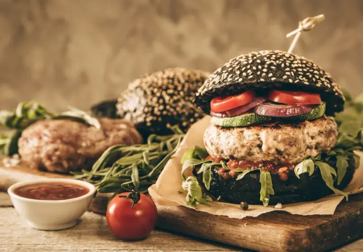 Soczysty burger z czarną bułką, kotletem, warzywami i sosem.