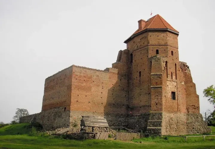Zamek w Liwie, ceglana twierdza z wieżą i dachem, stoi na wzgórzu.