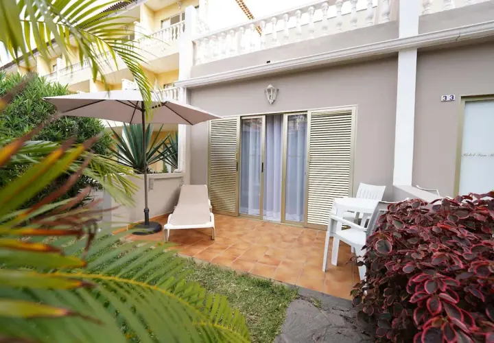 Terraza privada en el Hotel San Borondon con tumbona, sombrilla y mesa. Palmeras y vegetación exuberante rodean el espacio.