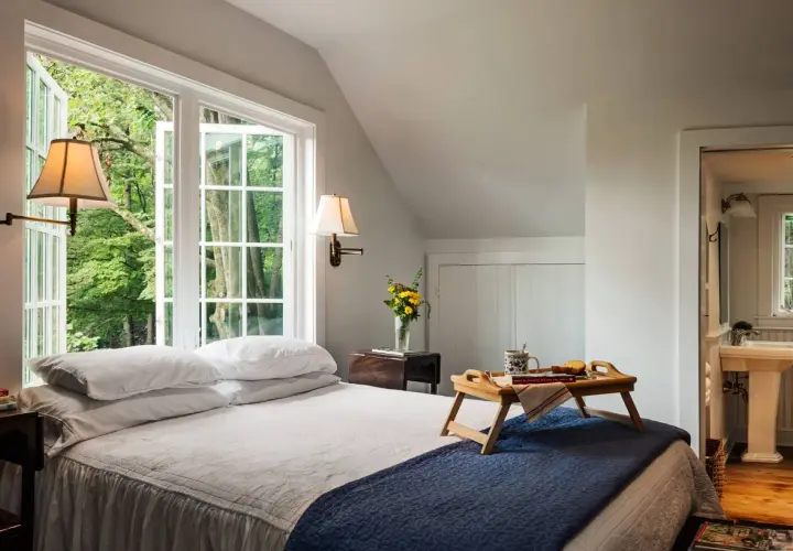 Cozy guest room decor with a bed, breakfast tray, and a window overlooking lush greenery.