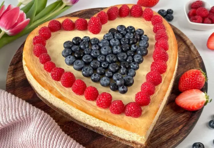 Herzförmiger Kuchen zum Muttertag, dekoriert mit Himbeeren und Blaubeeren. Ein süßes Dankeschön für Mama.