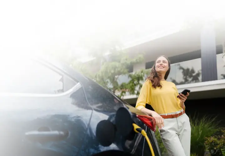 Mujer sonríe mientras carga su coche eléctrico, una elección sostenible que marca la diferencia entre híbrido y eléctrico.