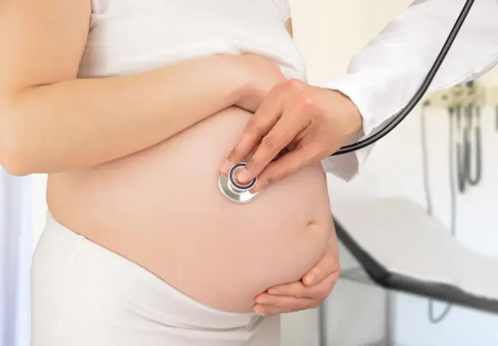 Medico ascolta battito fetale su pancia di donna incinta, controllo per gestosi gravidica.