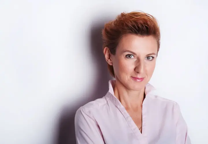 Kobieta z rudymi włosami w jasnoróżowej koszuli, uśmiecha się do obiektywu. Idealne miejsce do robienia zdjęć.
