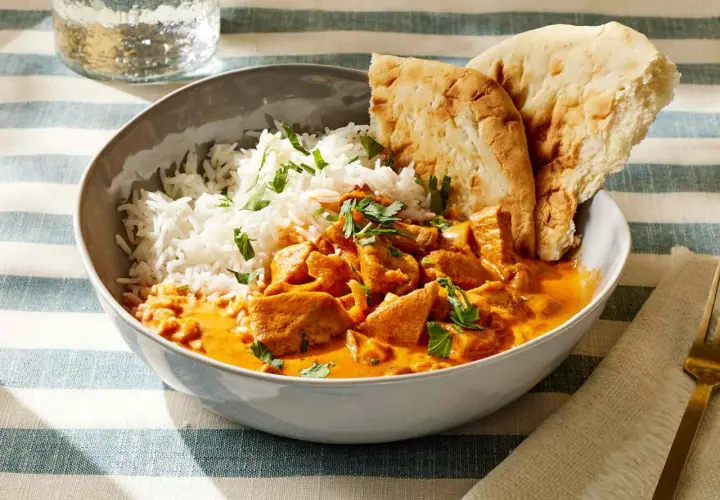 Miseczka pełna aromatycznego kurczaka butter chicken z ryżem i chlebkiem naan.