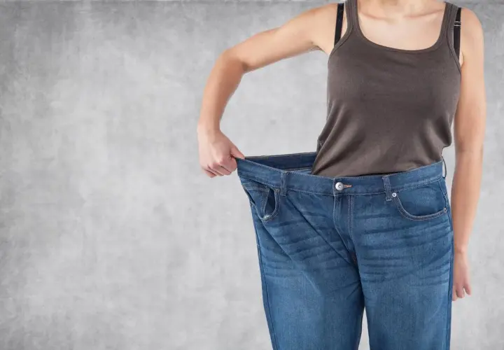 Erfolg beim Gewichtsverlust: Eine Person hält ihre viel zu große Jeans hoch, ein deutliches Zeichen für erreichten Gewichtsverlust.