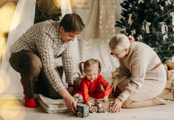 Rodzina podczas mini sesji świątecznej bawi się pociągiem pod choinką.
