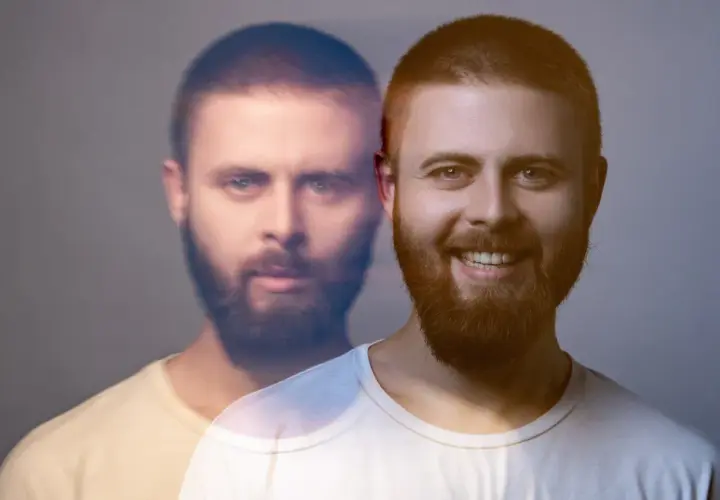 Dwóch mężczyzn z brodami, jeden uśmiechnięty, drugi z poważnym wyrazem twarzy, na szarym tle.