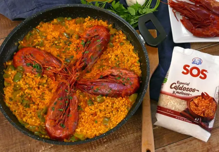 Arroz con carabineros en paellera, con pimientos verdes y perejil picado. A un lado, carabineros frescos y un paquete de arroz SOS.