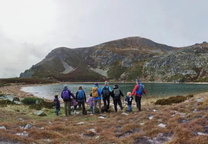 Un grupo de personas, incluyendo niños, disfruta de excursiones en familia junto a un lago rodeado de montañas.
