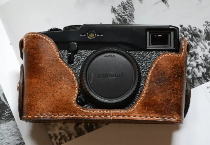 Skórzane etui na aparat Fujifilm X Pro1, z widocznym obiektywem X Mount, leży na stronach książki z historycznymi zdjęciami.