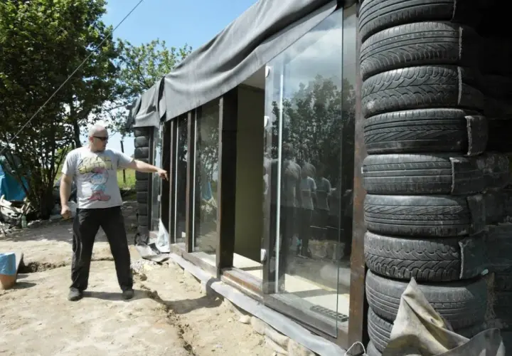 Budowa **earthship** z opon. Mężczyzna wskazuje na szklaną ścianę domu z opon.