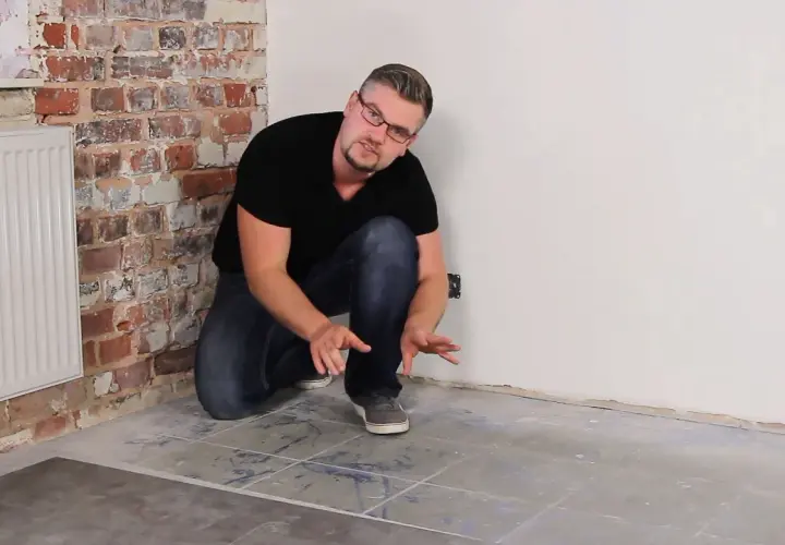 Uomo che mostra la posa pavimento pvc su pavimento esistente, con mattoni a vista e termosifone.