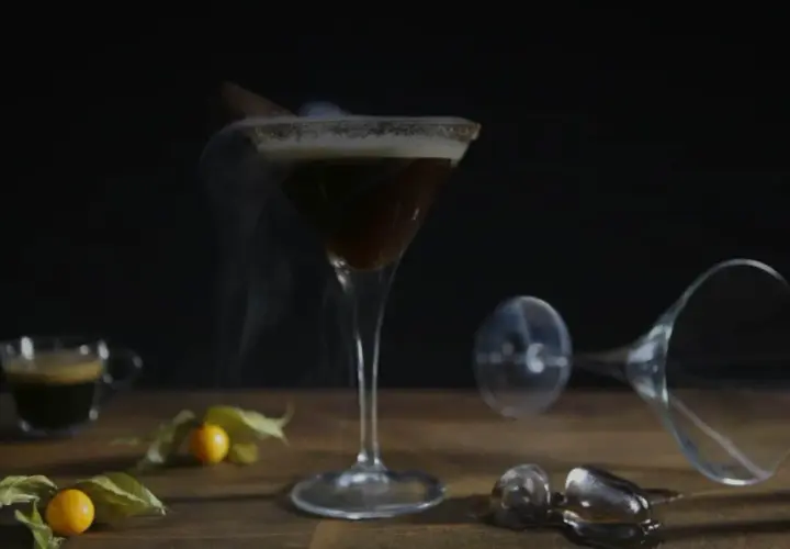 Ein dampfender Espresso Martini mit Zimt und einer kleinen Espressotasse daneben.