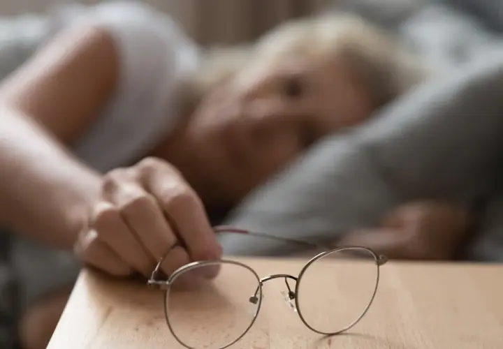 Kobieta sięga po okulary, czując wysokie tętno po przebudzeniu.