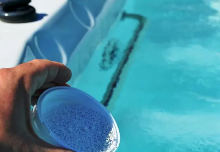 Dłoń wsypuje granulki bromu do błękitnej wody jacuzzi, dbając o czystość.