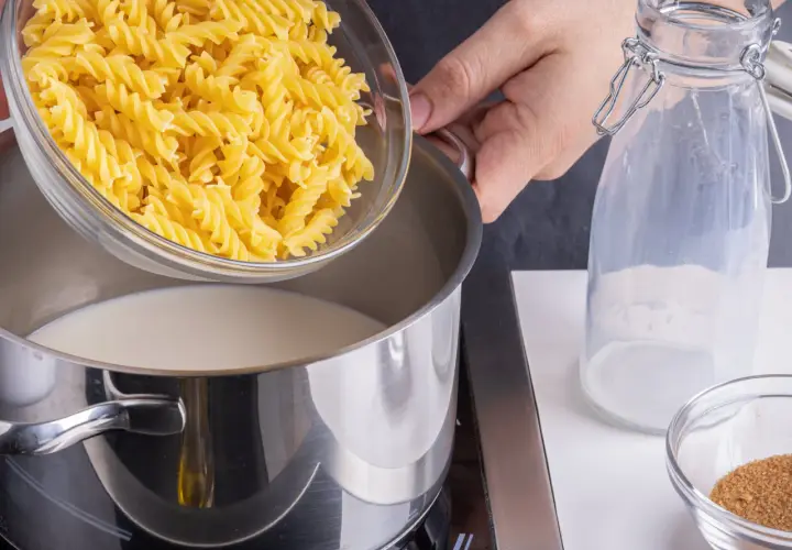 Eine Hand schüttet Spiralnudeln in einen Topf mit Milch. Zutaten für milch nudeln.