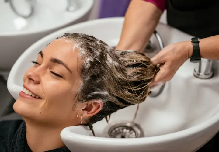 Una mujer sonríe mientras le lavan el pelo en un salón. La frecuencia con la que hay que lavarse el pelo varía, pero este momento de spa parece perfecto.