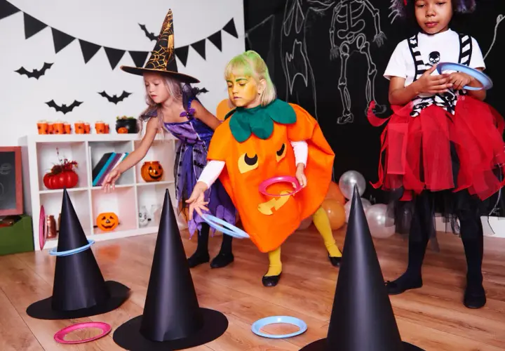Niñas disfrutan de una divertida celebración de Halloween lanzando aros a sombreros de bruja.