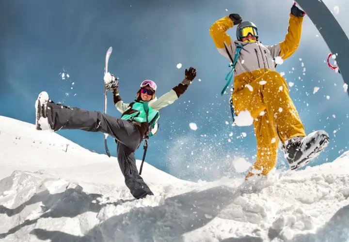 Dwóch narciarzy w akcji na śniegu, jeden z nartami, drugi na snowboardzie, z rozbryzgami śniegu.