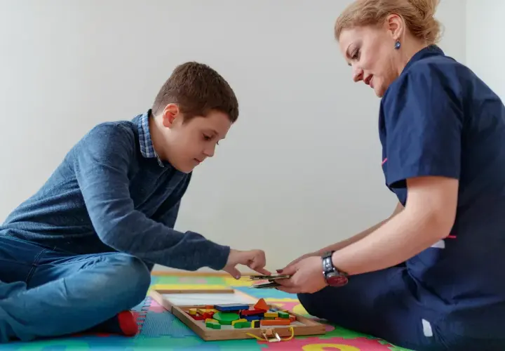 Chłopiec i terapeutka bawią się klockami w sali terapeutycznej.
