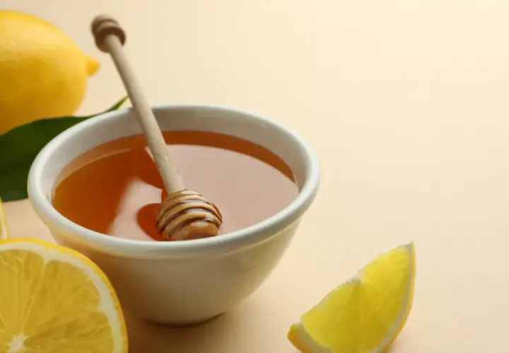Un remède naturel contre le mal de gorge : un bol de miel doré avec une cuillère en bois, entouré de citrons frais et de feuilles vertes.