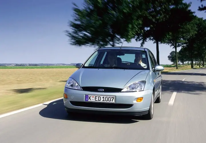 Srebrny Ford Focus MK1 1.6 benzyna w ruchu po wiejskiej drodze, z dwoma osobami w środku.