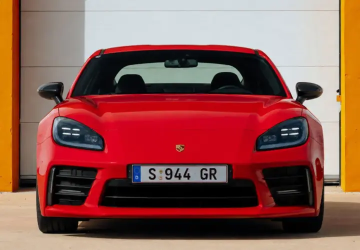 El llamativo Porsche 944 rojo, con su distintivo frontal y faros LED, se exhibe frente a una puerta de garaje blanca y paredes naranjas.